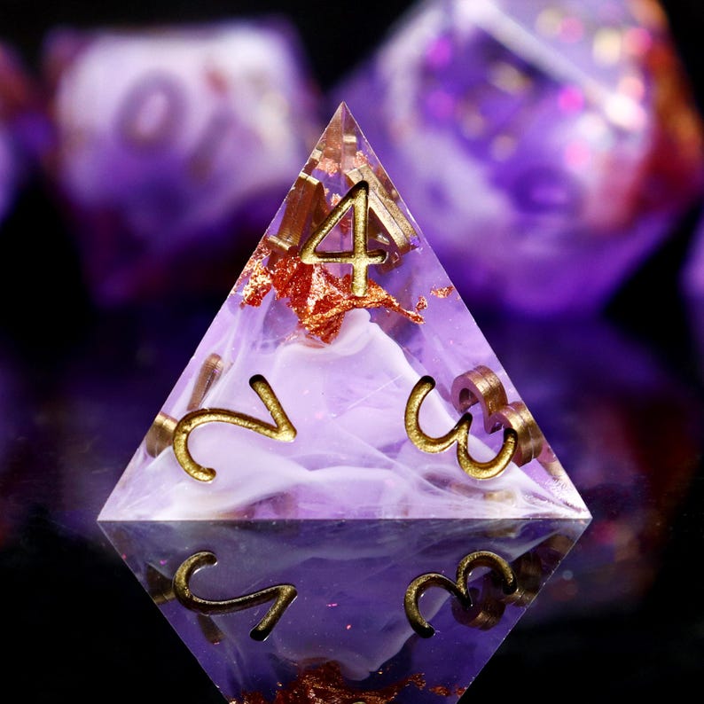 May include: A purple and white resin d4 dice with gold numbers 2, 3, and 4. The dice has a swirl pattern and gold flecks.