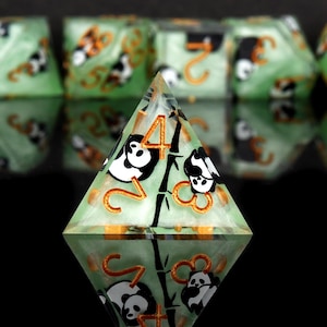 Könnte beinhalten: Ein grüner und weißer, schimmernder D20-Würfel mit schwarzen und weißen Pandabären und Bambus, die auf die Flächen gedruckt sind. Der Würfel hat goldene Zahlen und ist Teil eines Würfelsatzes.