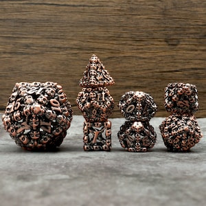 Puede incluir: Un conjunto de seis dados de cobre y plata con un diseño de calavera. Los dados están apilados en forma de torre.
