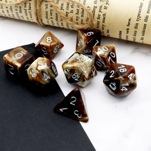 May include: A set of ten brown and white marbled dice with silver numbers. The dice are scattered on a white surface with a black surface in the background.
