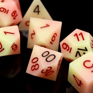 May include: A set of six dice with a yellow and pink gradient. The dice have black and red numbers on them. The dice are on a black surface.