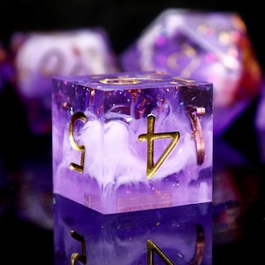 May include: A purple and white dice with gold accents and a swirl pattern. The dice has a symbol on one side.