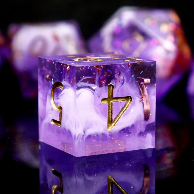 May include: A purple and white dice with gold accents and a swirl pattern. The dice has a symbol on one side.