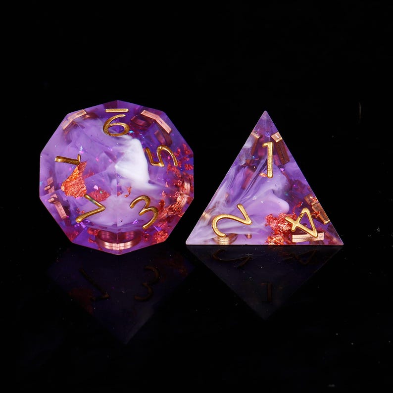 May include: Two purple dice with gold and white accents. The larger die is a 12-sided die with the numbers 1 through 12. The smaller die is a 4-sided die with the numbers 1 through 4.