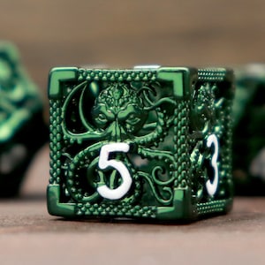 Puede incluir: Un dado de metal verde con un diseño detallado de una criatura con tentáculos y el número "5" en una de sus caras. El dado es parte de un conjunto de dados con diferentes números.