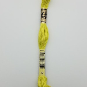 May include: A skein of bright yellow embroidery floss with a black and gold paper label. The label features the text DMC, 25, 8 m (8.7 yd), and the number 12. A barcode is printed on the lower section of the paper band wrapping the thread.