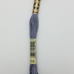 May include: A skein of DMC embroidery floss in a medium gray color, labeled number 414. The thread is wrapped in a paper band featuring the DMC logo, the text Moulin Special, and a length of 8 meters or 8.7 yards, along with a barcode.