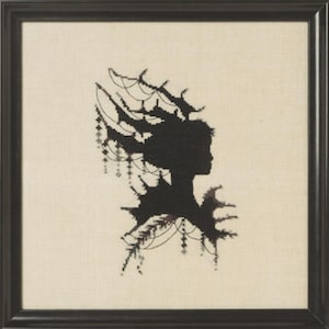 May include: A framed cross-stitch embroidery featuring a black silhouette of a profile head adorned with elaborate, branching antler-like structures and delicate hanging beaded chains, set against a plain, light beige fabric background.