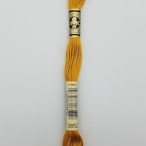 May include: A skein of golden yellow embroidery floss featuring a paper label with the text DMC, 25, 8m (8.7 yd), and the color number 3852. The thread is wound in a long, twisted loop, displaying a smooth, lustrous texture and a vibrant mustard hue.