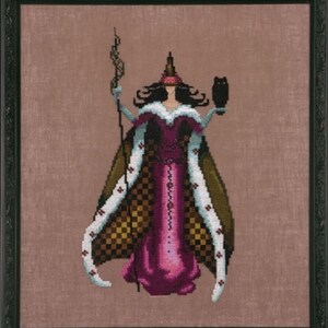 May include: A framed cross-stitch embroidery depicting a figure in a long magenta gown with a checkered pattern cape, white fur-like trim, and a pointed headpiece. The figure holds a tall, dark, twisted staff and a small black owl on one hand.