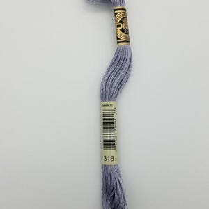 May include: A skein of light gray embroidery floss featuring a paper label with the text DMC, Mouliné, 25, 8m, 8.7yd, and the color number 318. The thread is wound into a long, twisted bundle, showcasing a smooth, matte texture and consistent color.