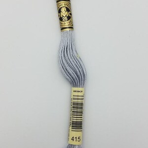 May include: A skein of light gray embroidery floss with a paper label featuring the text DMC, 25, 8m (8.7 yd), 6003042P, and 415. The thread is wound into a long, twisted bundle, showcasing a smooth, consistent texture and a metallic-like sheen.