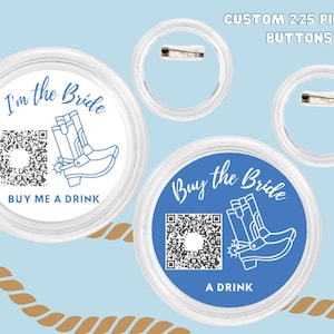 May include: Two 2.25 inch pinback buttons with a blue background and white text. One button says "Buy the Bride A Drink" and features a QR code and a pair of cowboy boots. The other button says "I'm the Bride" and features a QR code and a pair of cowboy boots.