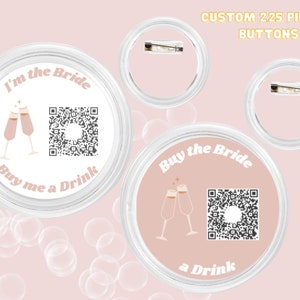May include: Two 2.25 inch pinback buttons with a pink background and white text. The first button says "I'm the Bride" with a champagne toast graphic and a QR code. The second button says "Buy the Bride a Drink" with a champagne toast graphic and a QR code.
