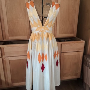 May include: A white sleeveless dress with a deep V-neckline and a geometric pattern of orange, yellow, and red diamonds. The dress has a fitted bodice and a full skirt.