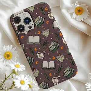 May include: A phone case with a repeating pattern of books, teacups, potion bottles, moons, and stars on a dark brown background. The case has a camera cutout and is surrounded by white daisies.
