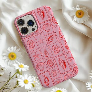 May include: A pink phone case featuring a red seashell design. The case has a camera lens cutout and a raised lip around the edges to protect the screen.