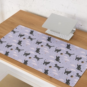 May include: A rectangular desk mat with a light purple background featuring a repeating pattern of black cat silhouettes, white clouds, stars, and crescent moons. A laptop and keyboard are on the wooden desk.
