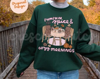 May include: A dark green sweatshirt with a graphic featuring two cartoon bears at a table with food and the text "Pumpkin Spice & Cozy Mornings". The design includes pumpkins and fall leaves.