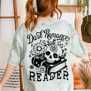 May include: A light green t-shirt with a black and white graphic design. The graphic features a skull with flowers, a book, and the text "Dark Romance Reader".