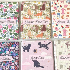 May include: Six decorative, rectangular boxes with various patterns and text labels. Designs include strawberries, cats, brunch items, floral patterns, cats with moons, and fantasy creatures. Labels read "Strawberry Fields", "Vintage Floral Cats", "Sunday Brunch", "Ditsy Florals", "Lunar Cats", and "Fantasy Reader".