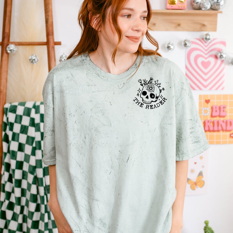 May include: A light green t-shirt with a distressed look featuring a black skull with flowers and the text "Only the reader" printed on the front.