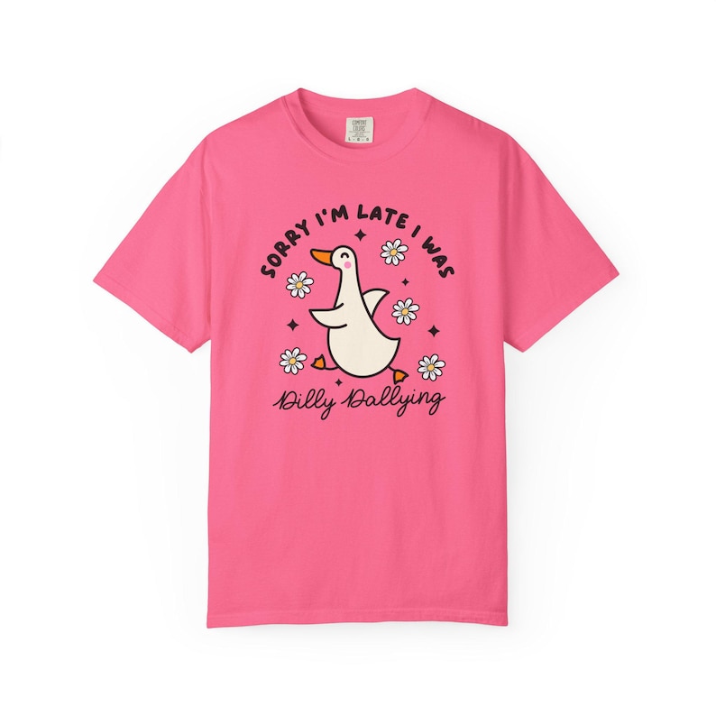 May include: Pink t-shirt with a cartoon duck graphic. The duck is white with an orange beak and feet, surrounded by daisies and the text "Sorry I'm late I was Dilly Dallying."