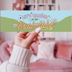 Könnte beinhalten: Ein blaues und grünes Lesezeichen mit dem Text "Let's wander in the bookstore, adventure awaits". Das Lesezeichen zeigt eine stilisierte Illustration eines grünen Hügels mit einer weißen Gänseblümchen und Sternen.