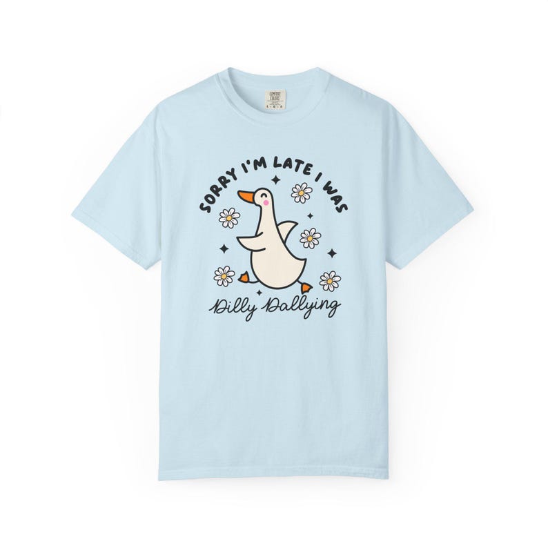 May include: Light blue t-shirt with a cartoon goose illustration. The goose is white with an orange beak and feet, surrounded by daisies and the text "Sorry I'm late I was dilly dallying."