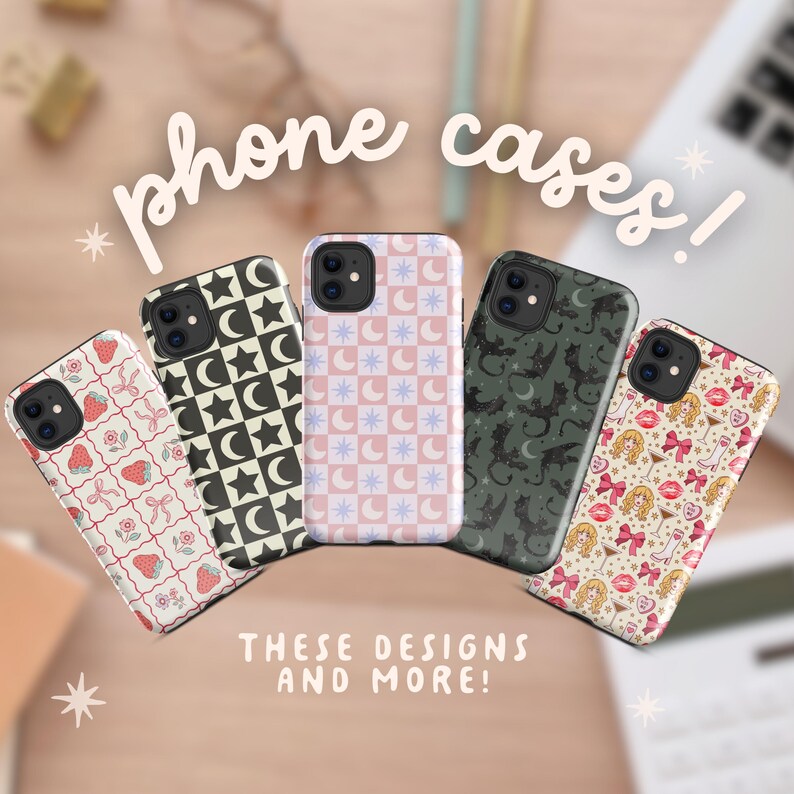 May include: A collection of phone cases with various designs, including strawberries, moons and stars, bats, and a pattern of bows and lips. The cases are in different colors, such as black, pink, and green. Text on the image reads "phone cases!" and "THESE DESIGNS AND MORE!"
