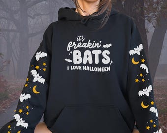 May include: Black hoodie with the text "it's freakin' BATS I LOVE HALLOWEEN" in white. The sleeves feature a pattern of white bats, yellow stars, and crescent moons. The hoodie has a front pocket and a hood.