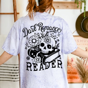 May include: A purple tie-dye t-shirt with a black and white graphic of a skull with flowers and books. The text "Dark Romance Reader" is printed on the shirt.