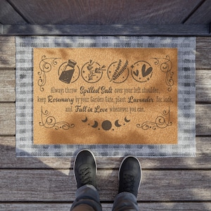 May include: A brown cork doormat with a white border and a black design. The design includes a bottle of salt, rosemary, lavender, and hearts. The text reads: "Always throw Spilled Salt over your left shoulder, keep Rosemary by your Garden Gate, plant Lavender for luck, and Fall in Love whenever you can."