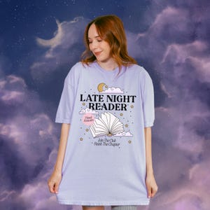 May include: A light purple t-shirt with the text "LATE NIGHT READER" and an illustration of an open book, moon, and stars. The shirt also includes the phrases "I Need Answers" and "Join The Club Finish The Chapter".