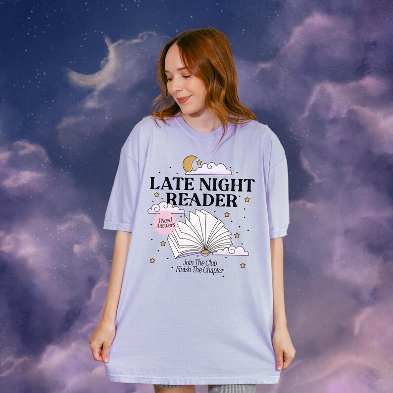 May include: A light purple t-shirt with the text "LATE NIGHT READER" and an illustration of an open book, moon, and stars. The shirt also includes the phrases "I Need Answers" and "Join The Club Finish The Chapter".