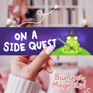 Könnte beinhalten: Ein lila-grüner Stoßfängermagnet mit einem Cartoon-Frosch, der einen Zaubererhut trägt und ein Schwert hält. Der Text auf dem Magneten lautet "On a Side Quest".