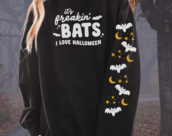 May include: Black sweatshirt with white text reading "it's freakin' BATS, I LOVE HALLOWEEN." The right sleeve has white bats, yellow crescent moons, and yellow stars. A Halloween-themed design.