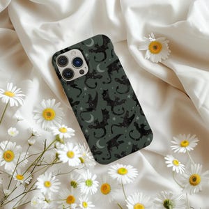 Puede incluir: Una funda de teléfono negra y verde con un patrón repetido de gatos negros y lunas crecientes. La funda está diseñada para un iPhone.