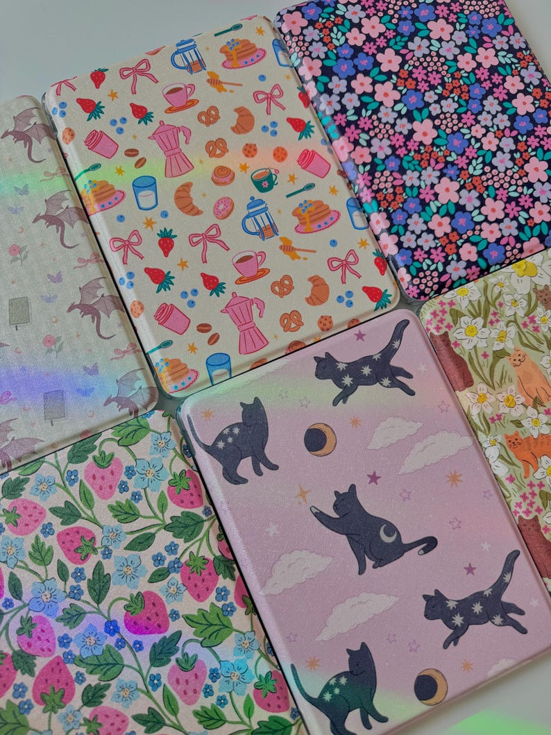 May include: A collection of patterned cases, featuring designs like floral, strawberries, cats with stars, and breakfast items. The cases have a glossy finish and a variety of colors, including pink, blue, and beige.