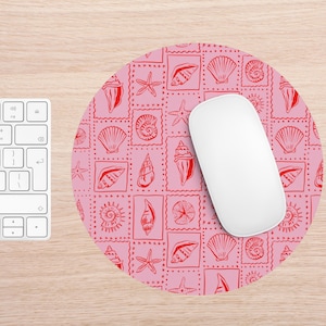 May include: A round pink mousepad with a red seashell pattern and a white computer mouse. The pattern features various seashell illustrations within red square frames. A white keyboard is visible on the left.