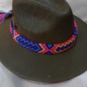 May include: A green woven hat with a colorful braided band. The band is made of pink, blue, and purple yarn.