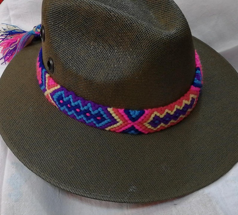 May include: A green woven hat with a colorful braided band. The band is made of pink, blue, and purple yarn.