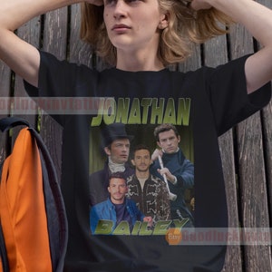 May include: A black t-shirt with a graphic print of Jonathan Bailey, an actor from the show Bridgerton. The graphic is a collage of images of Bailey in different scenes from the show. The text "Jonathan Bailey" is printed in green letters above the graphic, and the text "Bailey" is printed in green letters below the graphic.