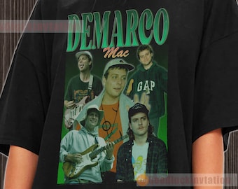 May include: Black t-shirt with a green graphic of musician DeMarco Mac. The graphic features a collage of photos of DeMarco Mac and his band members. The text "DEMARCO Mac" is printed in green letters on the shirt.