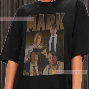 Peut inclure: T-shirt noir avec un imprimé graphique de quatre hommes. Le texte "MARK CORRIGAN" est imprimé sur le t-shirt.
