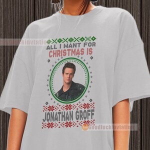 May include: A gray t-shirt with a Christmas-themed design featuring a portrait of Jonathan Groff. The text "All I want for Christmas is" is printed above the portrait.