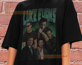 Puede incluir: Camiseta negra con un gráfico de estilo vintage de Luke Evans. El gráfico presenta múltiples imágenes de Luke Evans en diferentes poses y escenarios. El texto "LUKE EVANS" está escrito en una fuente retro en negrita.
