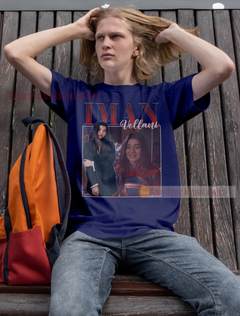 May include: A navy blue t-shirt featuring a photograph of Iman Vellani, the actress who plays Ms. Marvel, in a red and blue costume. The text "Iman Vellani" is printed in red on the shirt.