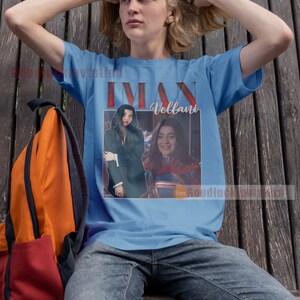 May include: A light blue t-shirt featuring a vintage-style image of two women. The image includes the text "Iman Vellani" and the Etsy logo.