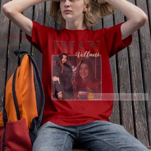 May include: Red t-shirt featuring a photograph of Iman Vellani, the actress who plays Ms. Marvel, in a superhero costume. The text "Iman Vellani" is printed on the shirt.